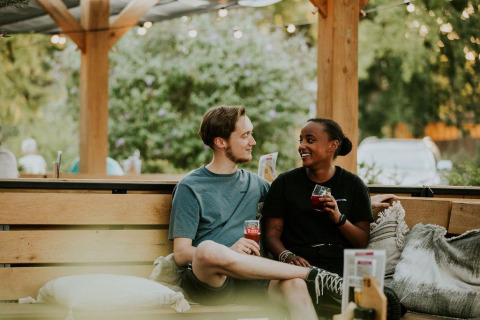 Dos personas sentadas en un banco exterior en un alojamiento glamping, compartiendo bebidas y sonrisas.