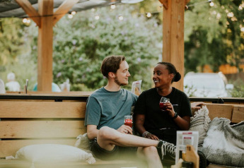 Deux personnes assises ensemble sur un banc extérieur dans un site de glamping, partageant des boissons et sourires.