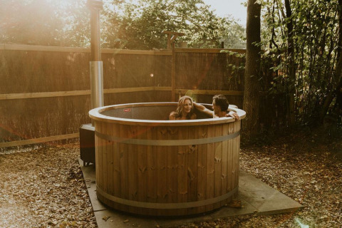 Couple relaxes in outdoor wooden hot tub at the Luxury Loft tiny house at Camping Si-Es-An, Netherlands.