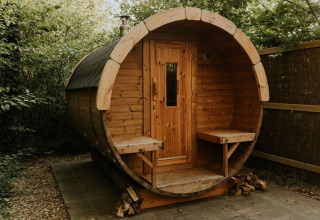 Casa pequeña de madera redonda con bancos, rodeada de vegetación en Camping Si-Es-An, Países Bajos.