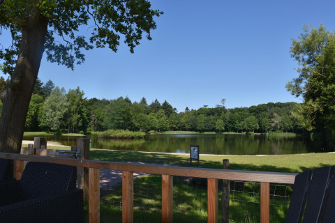 View from a terrace overlooking a serene lake and lush trees at Beach house with hottub at Camping 't Veld.