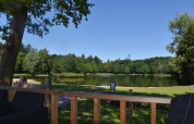 Udsigt over en idyllisk sø og grønne træer fra en terrasse ved strandhuset med spabad på Camping 't Veld.