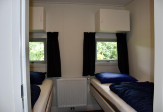 Dormitorio con dos camas individuales, cortinas oscuras y ventanas en un chalet de Camping 't Veld, Países Bajos.