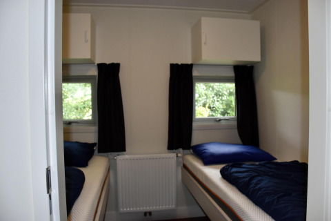 Schlafzimmer mit zwei Einzelbetten, dunklen Vorhängen und Fenstern im Chalet auf Camping 't Veld, Niederlande.