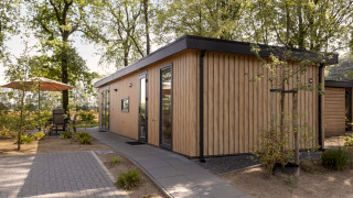 Moderne houten lodge Module Wood bij Bospark Ede in Nederland, omringd door bomen en een terras.