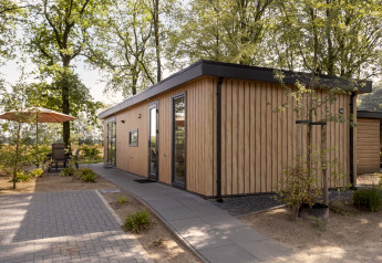 Moderna cabaña de madera llamada Module Wood en Bospark Ede, Países Bajos, rodeada de árboles y terraza.