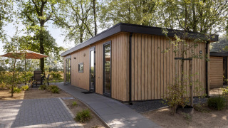 Modern wooden lodge called Module Wood at Bospark Ede in the Netherlands, surrounded by trees and a patio area.