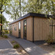Moderno lodge in legno chiamato Module Wood al Bospark Ede nei Paesi Bassi, circondato da alberi e patio.