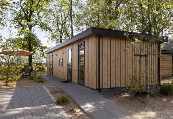 Moderne lodge af træ kaldet Module Wood ved Bospark Ede i Holland, omgivet af træer og terrassemøbler.