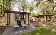 Moderne houten lodges met grote ramen en terrasstoelen in het groene Bospark Ede, Nederland.