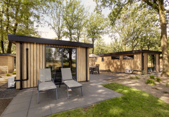 Cabañas modernas de madera con grandes ventanales y sillas en la terraza en Bospark Ede, Países Bajos.