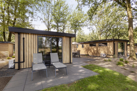 Modern wooden lodges with large windows and patio chairs surrounded by greenery at Bospark Ede, Netherlands.