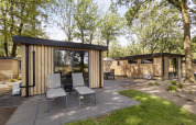 Lodges modernes en bois avec grandes fenêtres et chaises sur terrasse à Bospark Ede, Pays-Bas.
