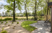 Outdoor view at Module Wood lodge in Bospark Ede, Netherlands, with lounge chairs and green forest.