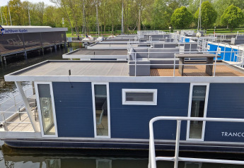 Houseboat named Havenlodge at Marina Parcs Naarden in the Netherlands, docked at the marina surrounded by trees.