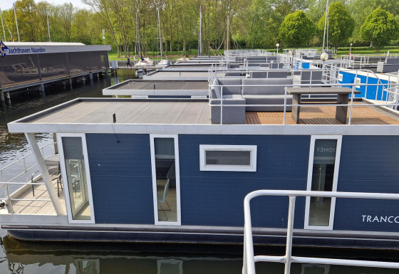 Husbåd navngivet Havenlodge ved Marina Parcs Naarden i Holland, fortøjet ved havnen med grøn omgivelse.