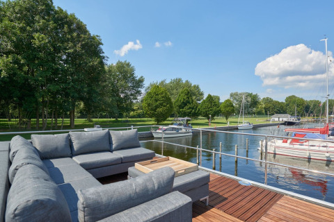 Terraza con sofá en un houseboat en Marina Parcs Naarden, Países Bajos, junto a barcos y naturaleza.