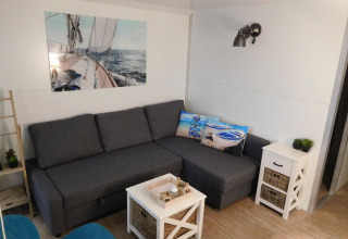 Lichte, moderne woonkamer op een woonboot bij Marina Parcs Naarden met grijze bank en nautische decoratie.