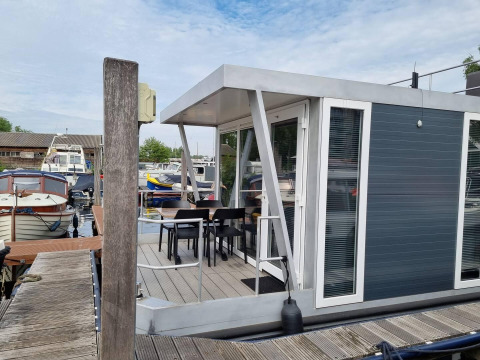 Casa flotante moderna con terraza y sillas en Marina Parcs - Jachthaven De Hoop, rodeada de barcos.