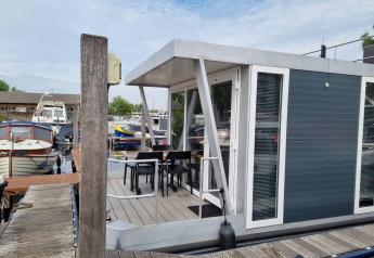 Moderne husbåd med terrasse og stole ved Marina Parcs - Jachthaven De Hoop i Holland, omgivet af både.