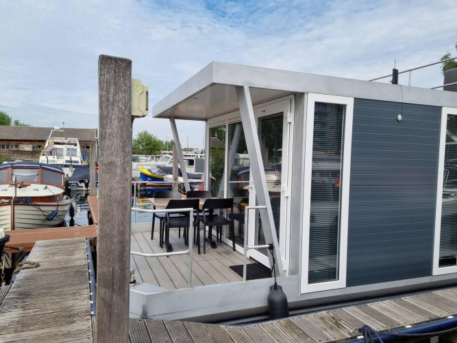 Moderne Hausboot mit Terrasse und Stühlen im Jachthafen De Hoop, umgeben von anderen Booten in Holland.