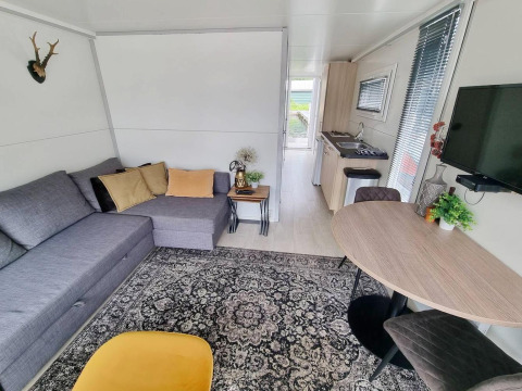 Salón moderno en la casa flotante 'De Hoop' en Marina Parcs, con sofá gris, alfombra y cocina.