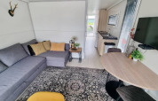 Salón moderno en la casa flotante 'De Hoop' en Marina Parcs, con sofá gris, alfombra y cocina.