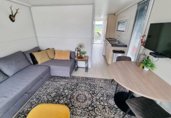 Salón moderno en la casa flotante 'De Hoop' en Marina Parcs, con sofá gris, alfombra y cocina.