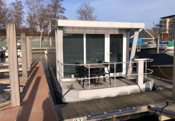 Modern houseboat docked at Marina Parcs - Jachthaven De Hoop, Netherlands, featuring outdoor seating area.