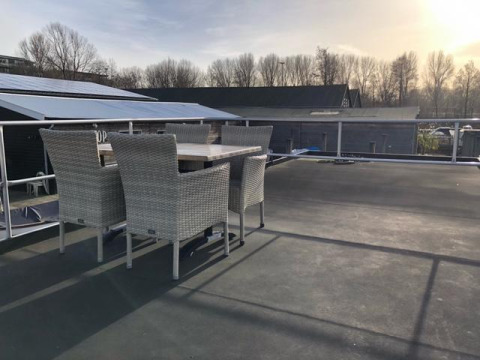 Tagterrasse på husbåd De Hoop med udendørs spisebord og stole ved Marina Parcs i Holland, solrig dag.