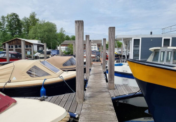 Wooden dock between moored boats at Marina Parcs, with Houseboat 'De Hoop' visible in the Netherlands.