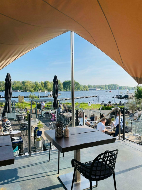 Udsigt fra et husbåd-caféområde ved Marina Parcs - Jachthaven De Hoop, med udsigt over vandet og naturen.