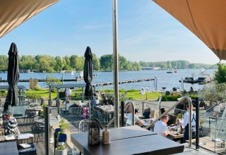 Zicht vanop een woonboot bij Marina Parcs - Jachthaven De Hoop, met een terras aan het water in de zon.