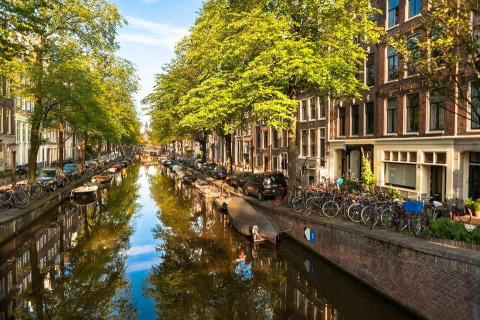 Vista desde la casa flotante De Hoop en Marina Parcs, Ámsterdam, con canal, botes, árboles y bicicletas.