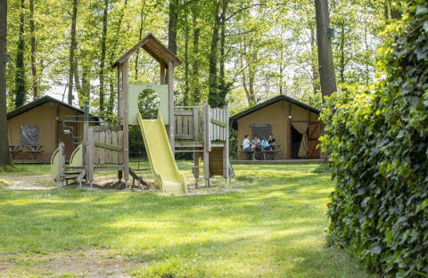 Spielplatz mit Rutsche vor Safarizelten im Grünen im Recreatiepark Den Blanken, Niederlande.