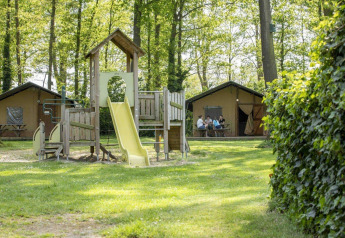 Parque infantil con tobogán frente a tiendas safari en un entorno verde en Recreation Park Den Blanken, Países Bajos.