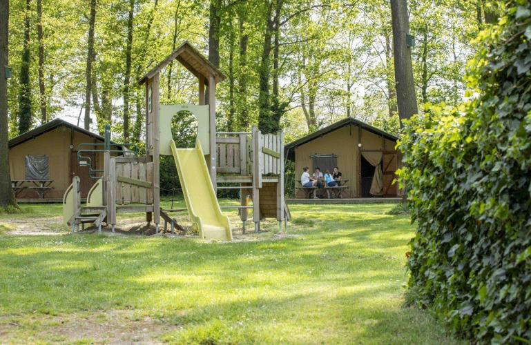Parque infantil con tobogán frente a tiendas safari en un entorno verde en Recreation Park Den Blanken, Países Bajos.