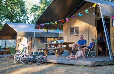 Familie entspannt vor einem Safarizelt im Recreation Park Den Blanken, Niederlande, mit Fahrrädern und Girlanden.