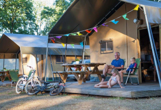 Familia relajándose frente a una tienda safari en Recreation Park Den Blanken, Países Bajos, con bicicletas y banderines.
