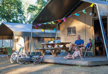 Familie entspannt vor einem Safarizelt im Recreation Park Den Blanken, Niederlande, mit Fahrrädern und Girlanden.