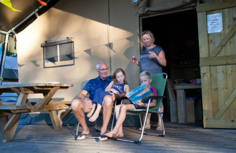 Familie entspannt vor einem Safarizelt im Recreation Park Den Blanken, Niederlande, Kinder lesen Buch.