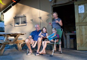 Famiglia si rilassa davanti a una tenda safari al Recreation Park Den Blanken, Paesi Bassi, bambini leggono.