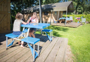 Due bambini seduti a un tavolo da picnic blu davanti a una tenda safari al Recreation Park Den Blanken, Paesi Bassi.