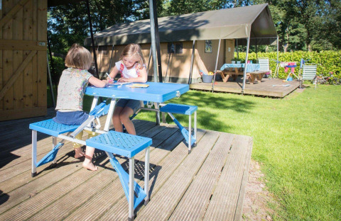 Due bambini seduti a un tavolo da picnic blu davanti a una tenda safari al Recreation Park Den Blanken, Paesi Bassi.