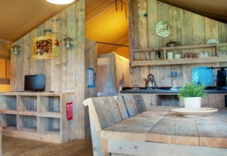 Vista interna di una tenda safari al Recreation Park Den Blanken, con mobili rustici in legno e cucina.