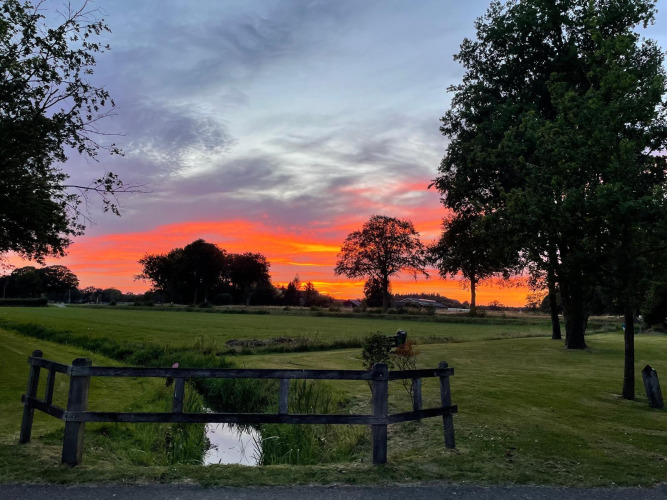Atardecer colorido sobre campos y árboles visto desde la tienda safari en Recreatiepark Den Blanken, Países Bajos.