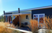Cabaña Comfort Lodge en Kompas Camping - Westende, Bélgica, rodeada de hierbas altas y cielo azul brillante.