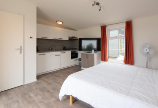 Interior de la tiny house Comfort Lodge en Kompas Camping Westende, Bélgica, con cama, cocina y televisor.