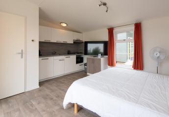 Interior de la tiny house Comfort Lodge en Kompas Camping Westende, Bélgica, con cama, cocina y televisor.