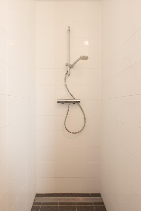 Eenvoudige douche met witte tegels in de badkamer van Comfort Lodge tiny house, modern en functioneel.